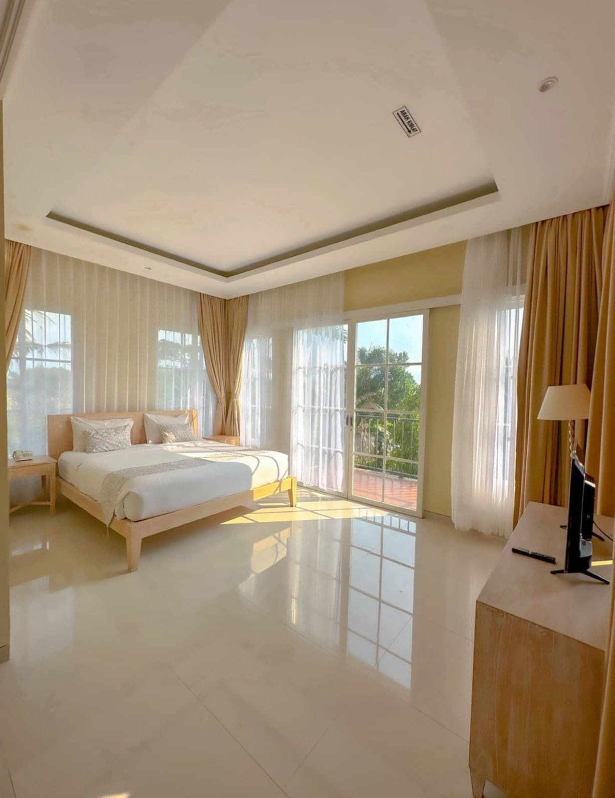 A spacious bedroom with a large bed, a bedside table, and a view of greenery through the window.