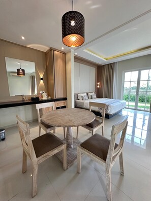 A modern hotel room with a round dining table, wooden chairs, a large bed, and a balcony with a view. - Sevilla Resort Magelang (Mungkid)