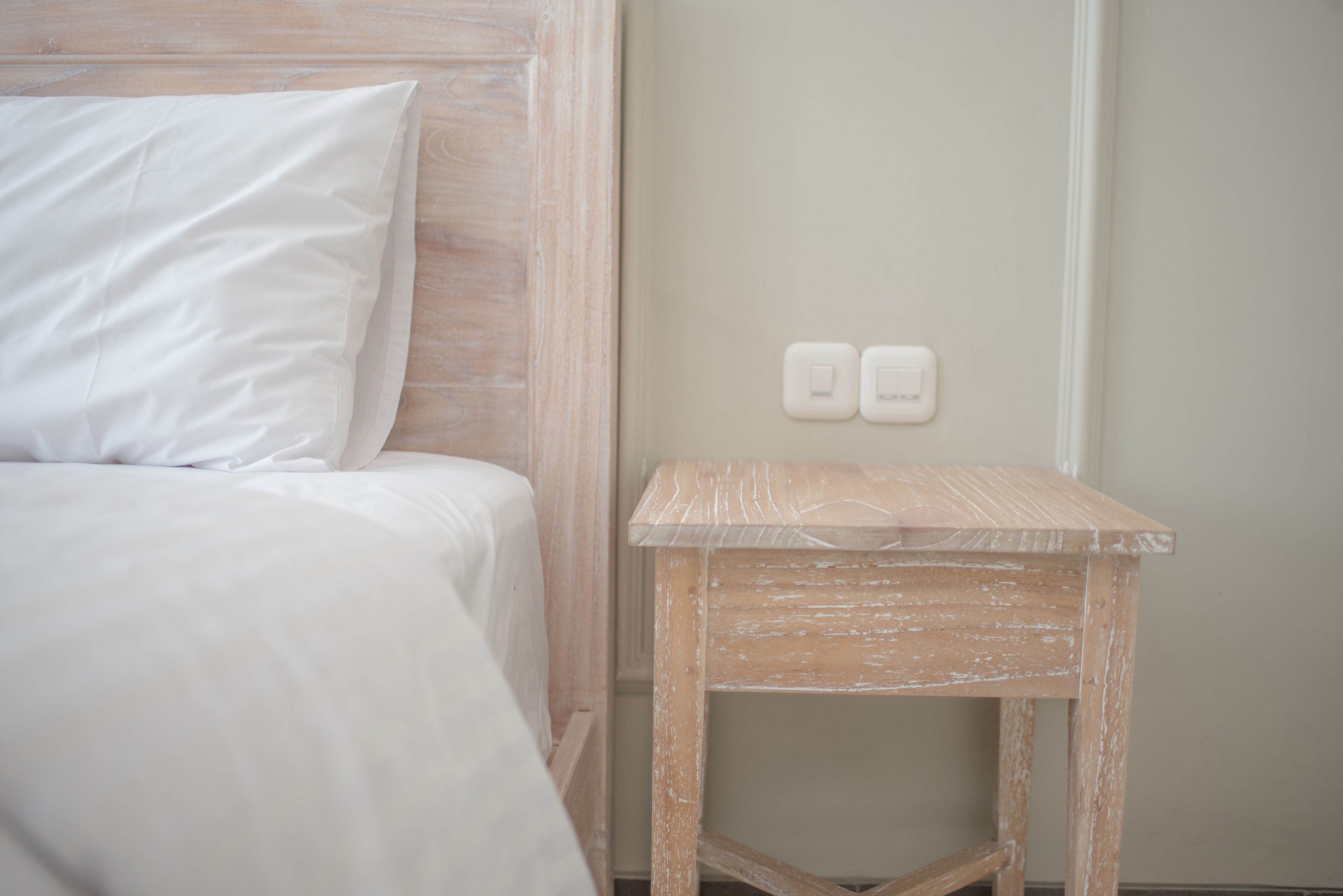 A bedroom with a bed, a wooden nightstand, and two wall-mounted light switches.