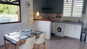 A compact kitchen with a washing machine, a dining table with chairs, and a window with blinds.
