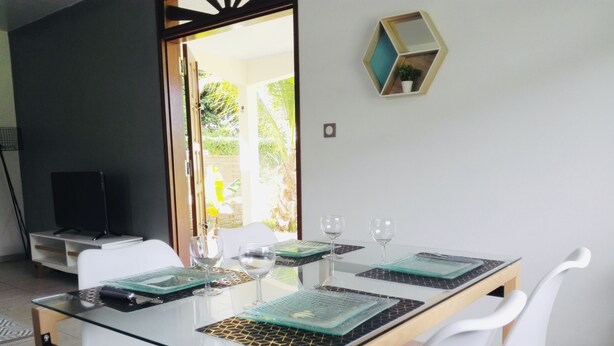 A dining area with a glass table, white chairs, and a TV in the background.