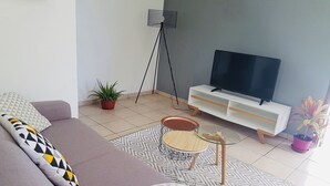 A modern living room with a grey sofa, a glass coffee table, a white TV stand, and a floor lamp.