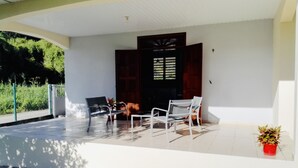 A covered outdoor seating area with two metal chairs and a small table, a potted plant, and a door with a window.
