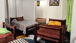 Una habitación con dos camas de madera, una con ropa de cama a rayas y otra con ropa de cama lisa. Hay una cortina verde a la derecha.