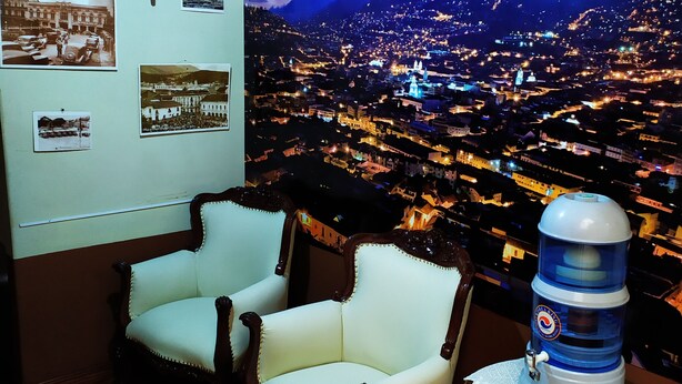 Una habitación con dos sillones, un dispensador de agua y una pared decorada con fotografías enmarcadas.