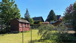 A grassy area with a small wooden shed, a fenced area, and houses in the background. - Apartment in the city and nature (Kierspe)