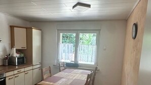 A compact kitchen with wooden cabinets, a dining table, and a window with curtains. - Apartment in the city and nature (Kierspe)
