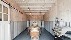 A rustic interior with a wooden barrel centerpiece, a grill station, and a long table with chairs. - Historic 1910 Bungalow & Carriage House • Dog Friendly • 1 Block to Wine & Dine (McMinnville)
