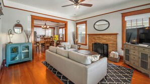 A living room with a sofa, a fireplace, a television, and a ceiling fan. - Historic 1910 Bungalow & Carriage House • Dog Friendly • 1 Block to Wine & Dine (McMinnville)
