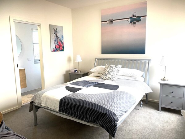 A modern bedroom with a bed, bedside tables, a nightstand, a mirror, and artwork on the walls.