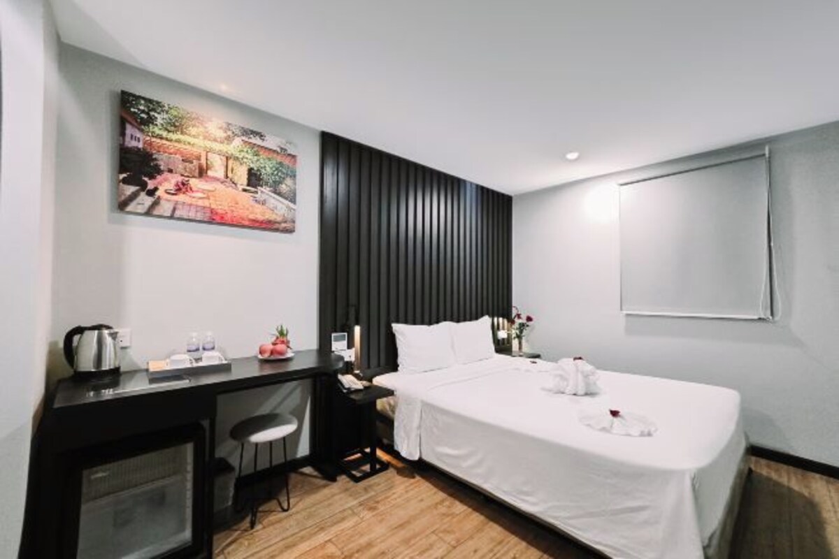 Camera d'albergo moderna con un letto, una scrivania con un computer, una sedia, un angolo cottura e un quadro appeso al muro.