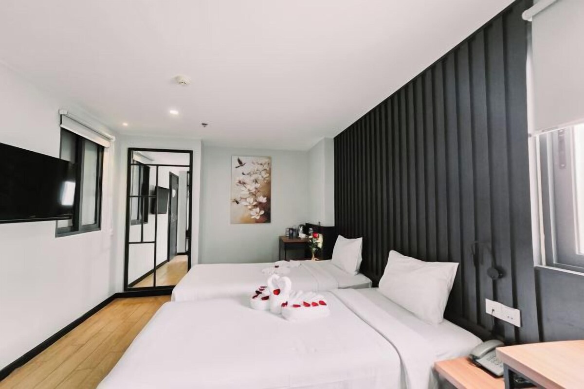 A modern hotel room with a large bed, a flat-screen TV, a bedside table, and a mirror.