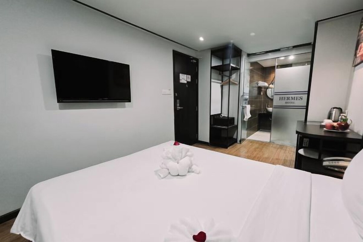 A hotel room with a bed, a flat-screen TV mounted on the wall, a closet, and a bathroom visible through a glass door.