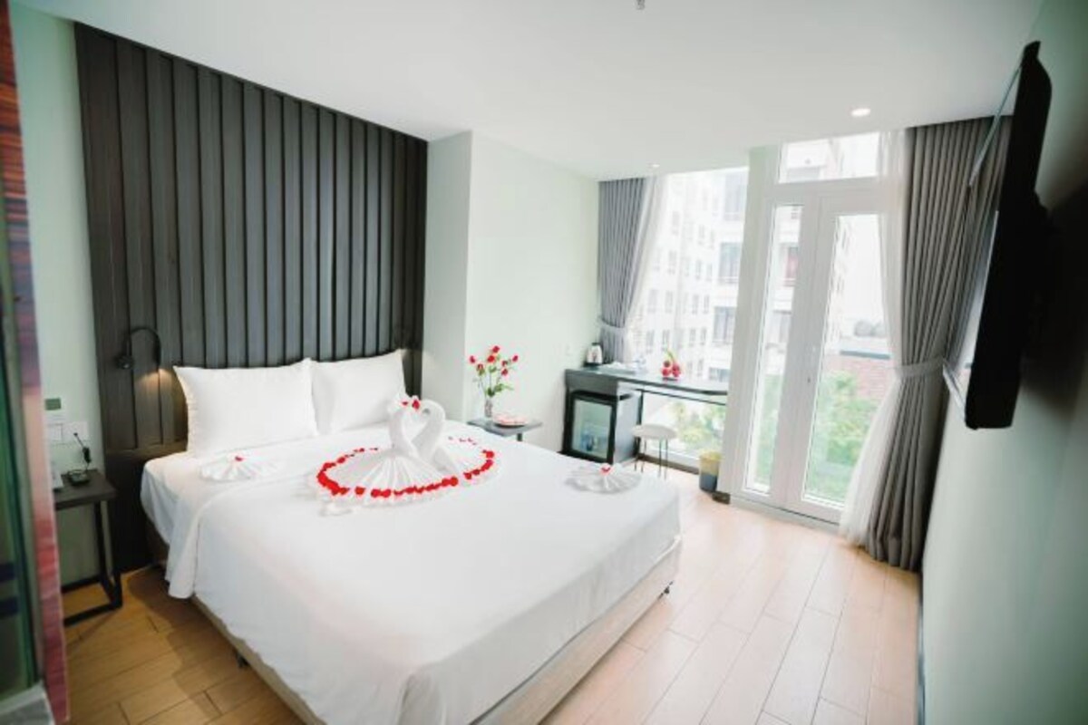 Camera d'albergo con un letto grande, una scrivania con una sedia, una TV a parete e una finestra con tende.