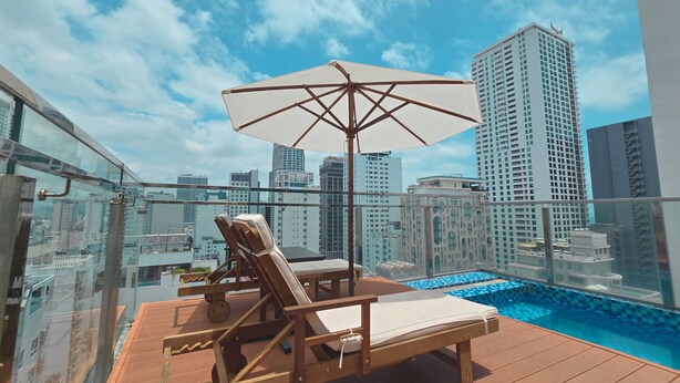 A rooftop pool area with lounge chairs and an umbrella, overlooking a cityscape with high-rise buildings. - Hermes Hotel Nha Trang (Nha Trang)