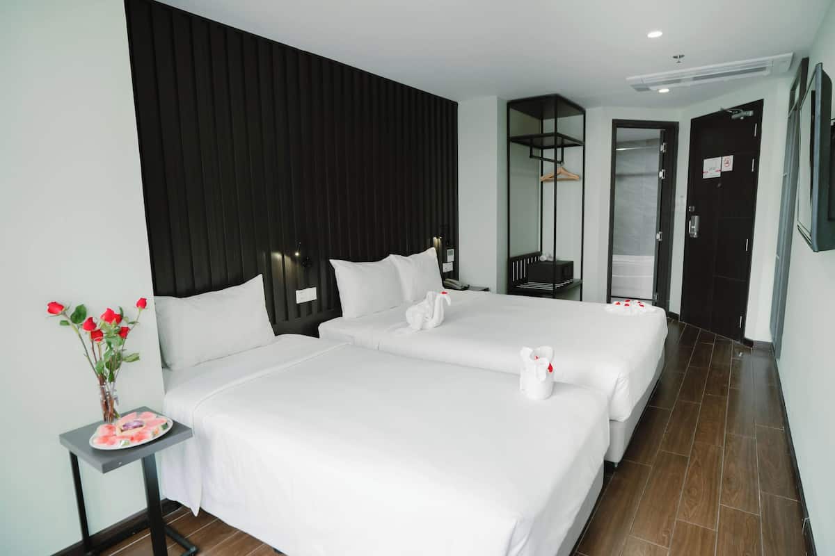 A hotel room with two beds, a small table with a vase of flowers, and a mirror on the wall.