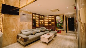 A modern living room with a sectional sofa, a flat-screen TV mounted on the wall, and a painting of flowers. - Hermes Hotel Nha Trang (Nha Trang)