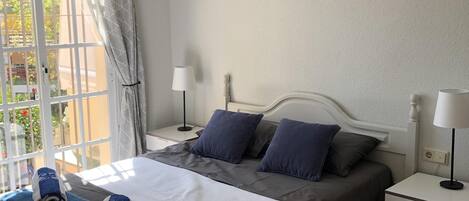 A bedroom with a bed, two bedside tables, a window with curtains, and a wall-mounted heart-shaped decoration.