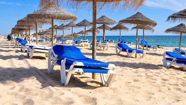 Een strand met rijen ligbedden en rieten parasols.