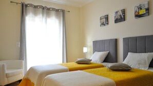 Een hotelkamer met twee bedden, een stoel en een raam met gordijnen.