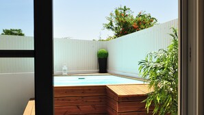 Een houten terras met een jacuzzi, een kleine tuin en een uitzicht op de lucht door een raam.