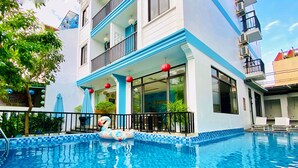 A swimming pool with a decorative flamingo float, surrounded by a building with balconies and large windows. - Grand Holiday Villa (Da Nang)