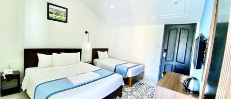 A hotel room with two beds, a desk, a chair, a small table, a lamp, and a picture on the wall.