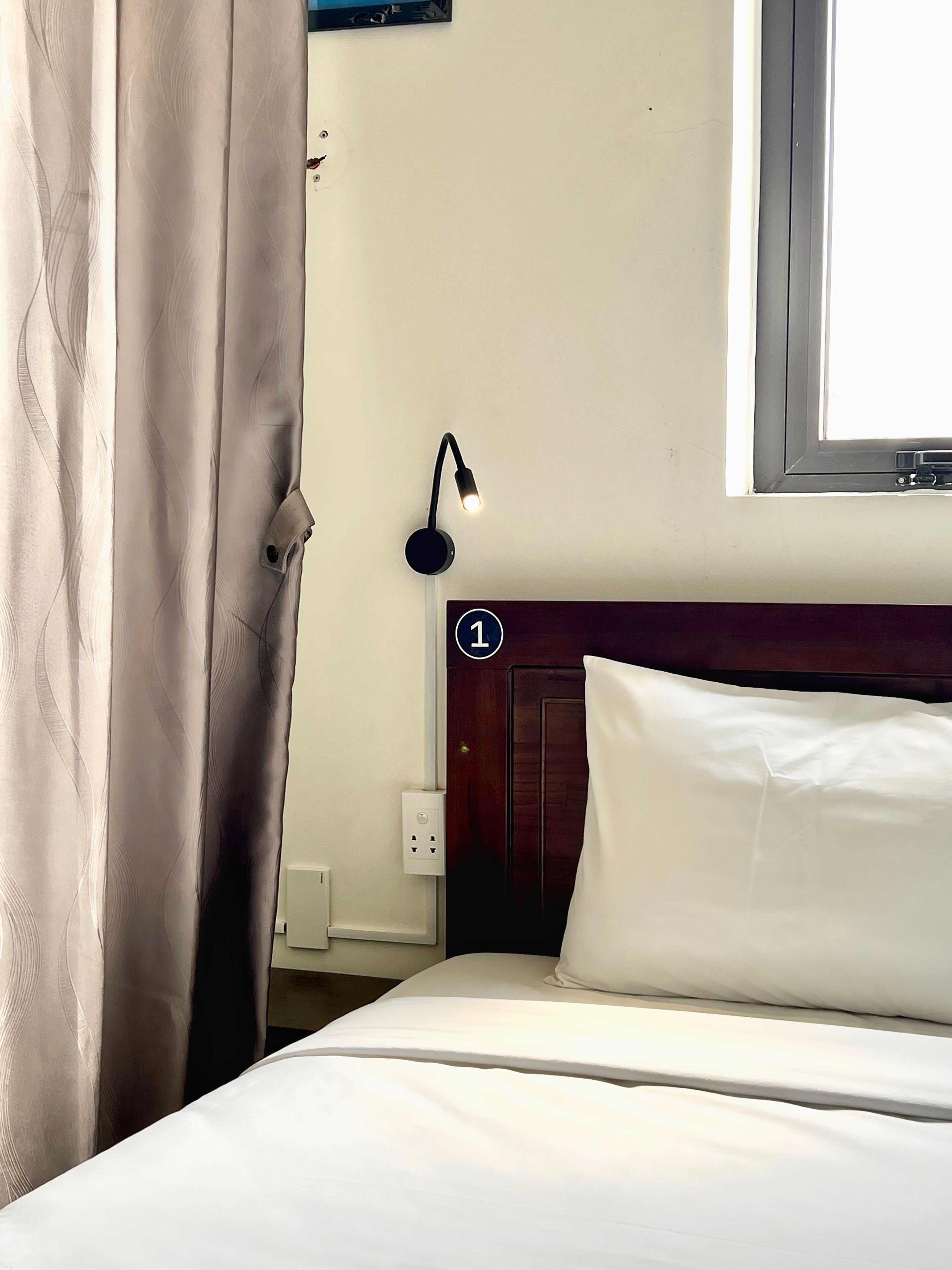 A hotel room with a bed, a nightstand, a lamp, a window, and a door.