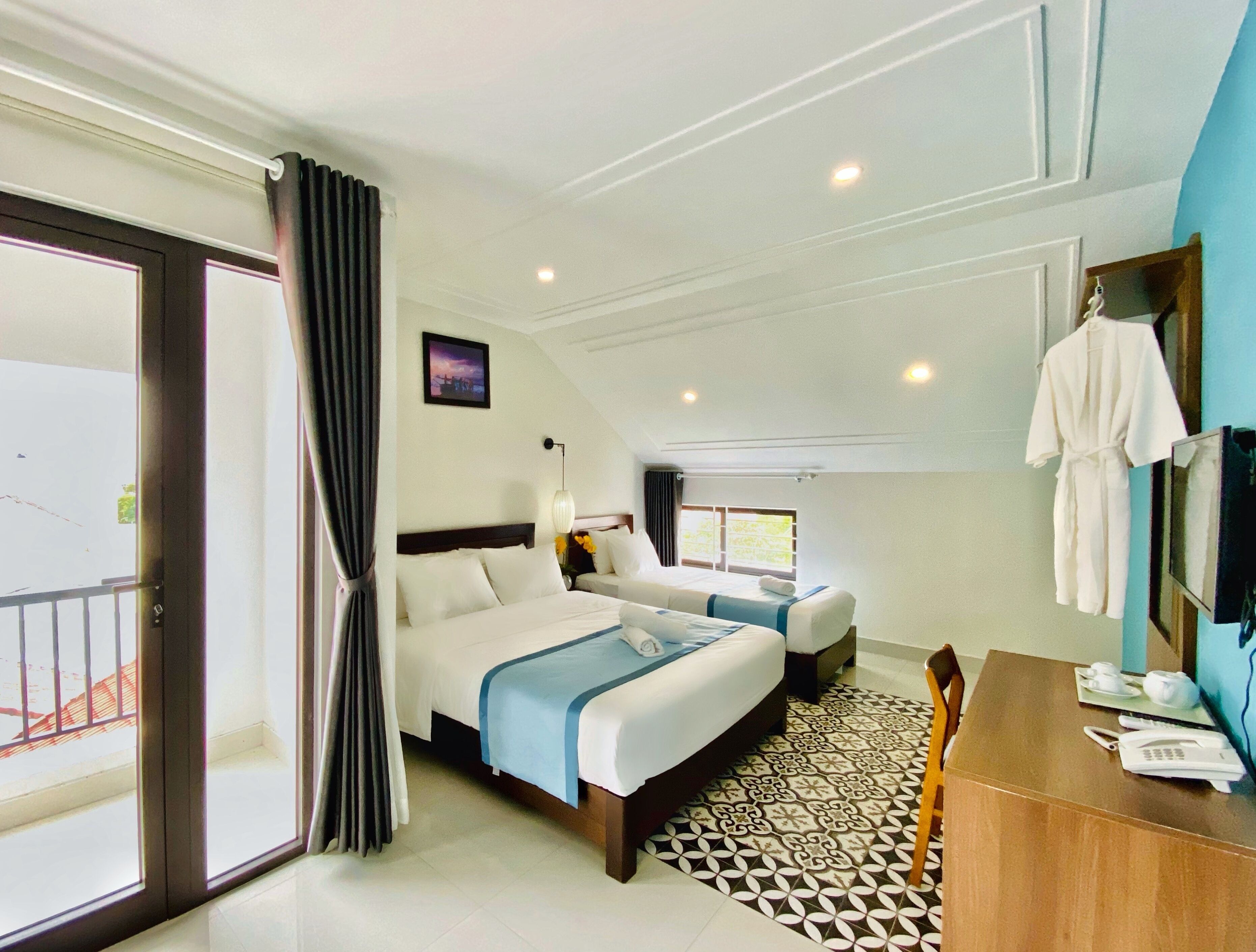 Quarto de hotel com uma cama grande, uma cama menor, uma mesa com telefone e vista para o exterior.