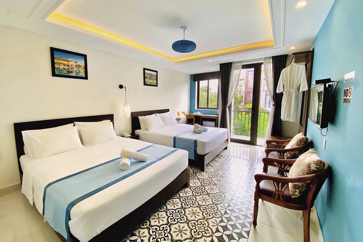 A hotel room with two beds, a desk, a chair, a balcony with a view, and a no-smoking sign.