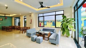 A spacious living room with a large window, a ceiling fan, and a dining area with wooden furniture. - Grand Holiday Villa (Da Nang)