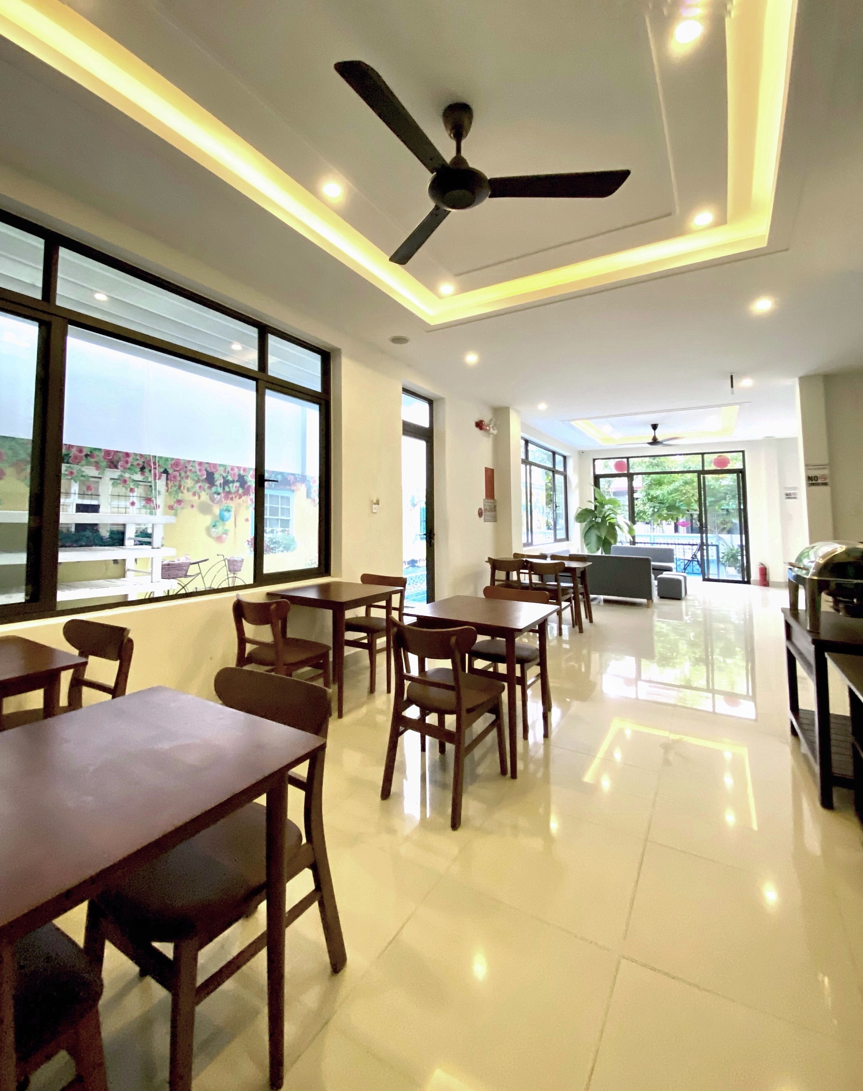 A spacious dining area with wooden tables and chairs, large windows, and ceiling fans.