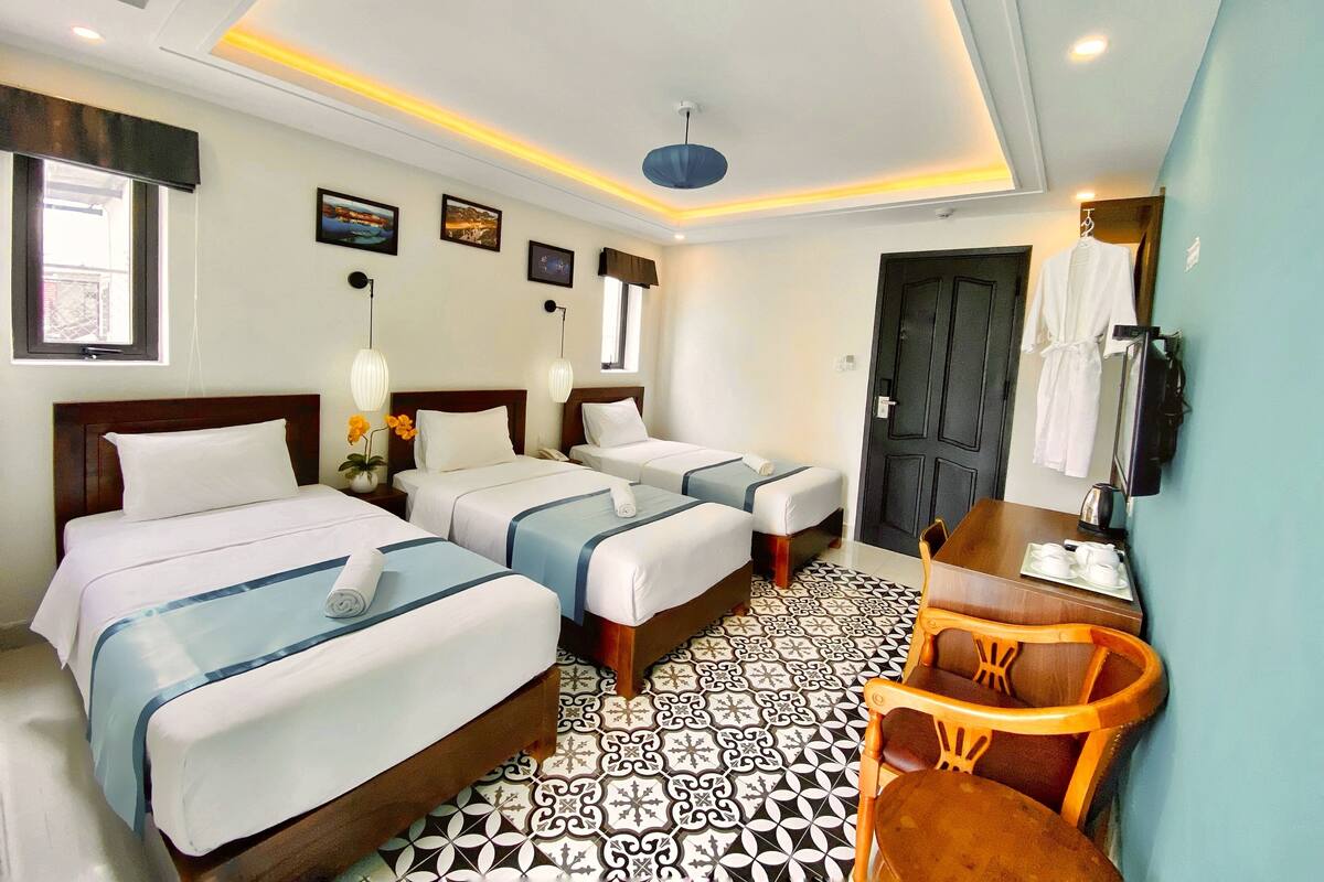 A hotel room with two beds, a desk, a chair, a TV, and a door.