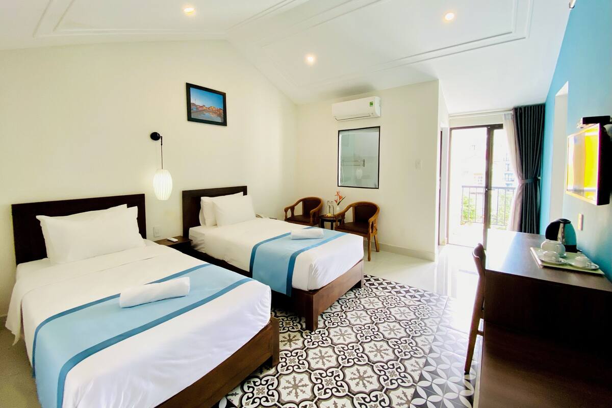 A hotel room with two beds, a desk, a chair, and a view of the outdoors.