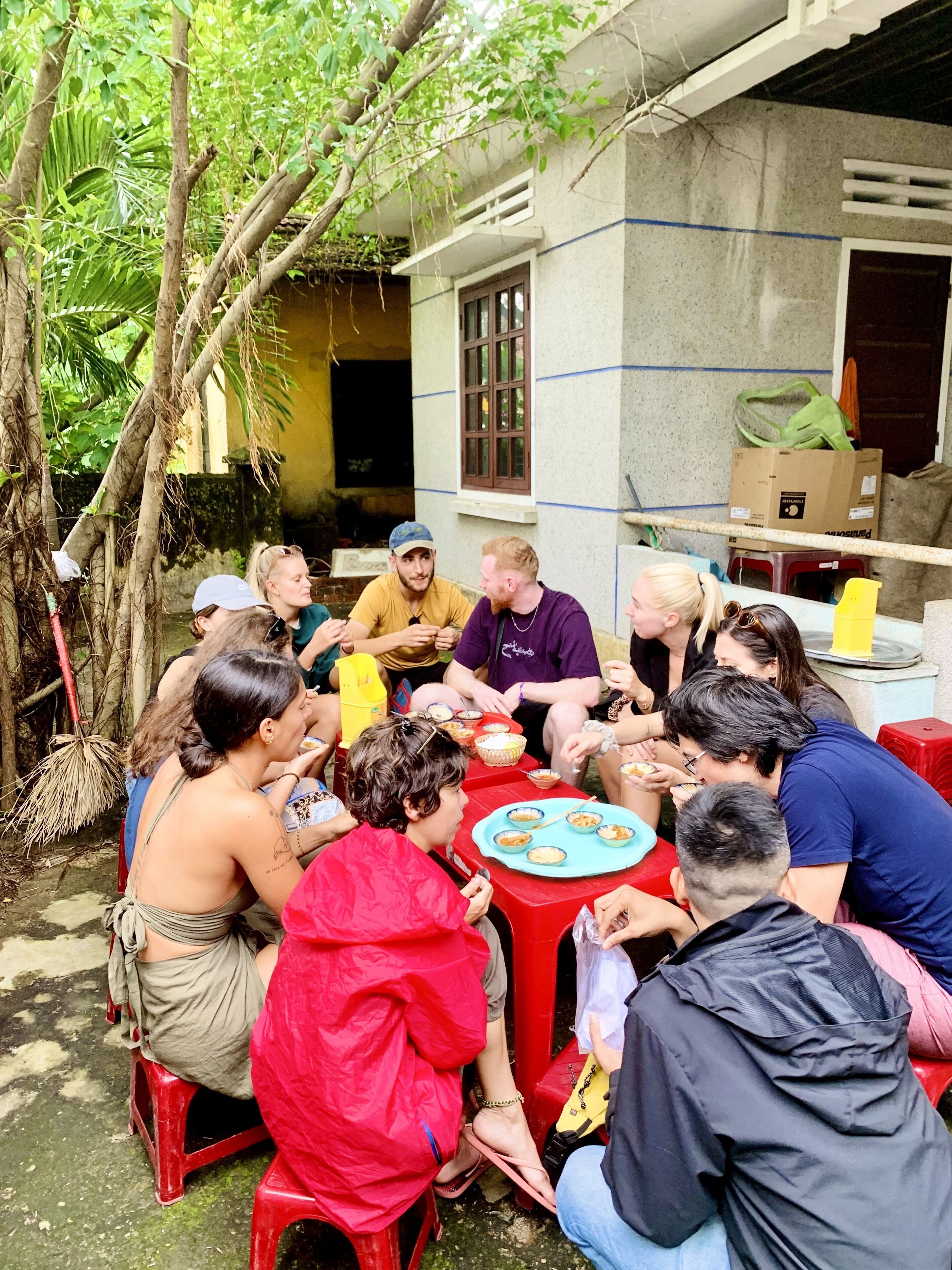A group of people seated around a table outdoors, engaged in a meal.