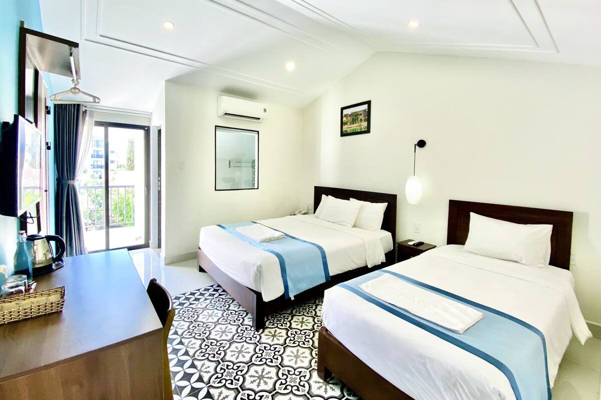 A hotel room with two beds, a desk, a chair, a TV, and a window with curtains.