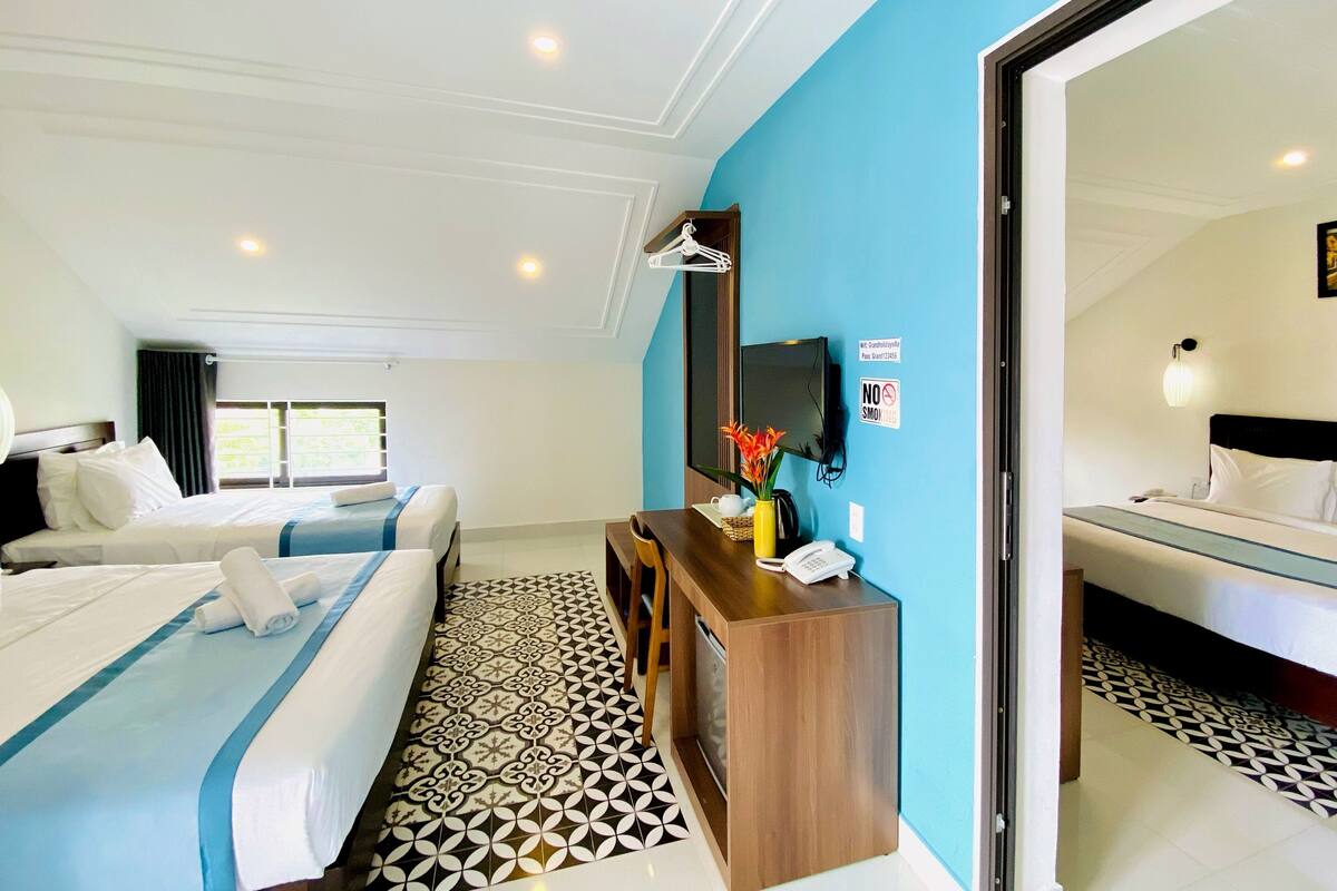 A hotel room with two beds, a desk, a TV, and a bathroom visible through an open door.