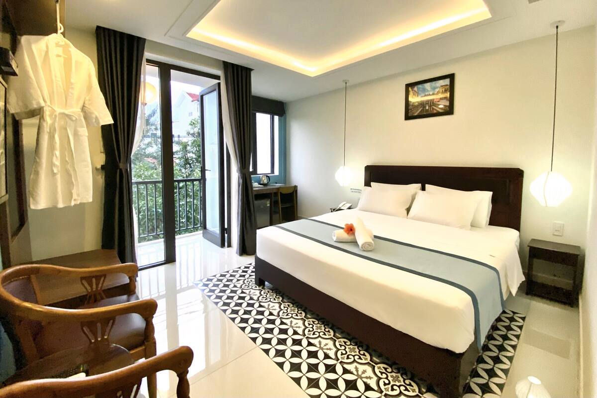 A hotel room with a large bed, a desk, a chair, and a balcony with curtains.