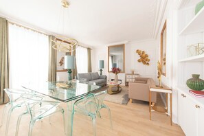 A modern living room with a glass dining table, clear chairs, a grey sofa, and a beige armchair. - Beaubois, 2BR/3BA, 6 people (París)