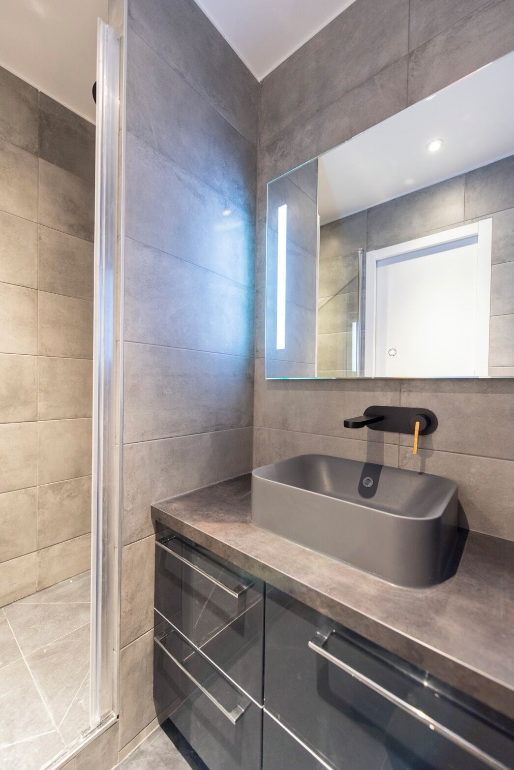 A modern bathroom with a glass shower enclosure, a stainless steel sink, and a large mirror.