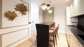 A modern kitchen with a black countertop, a dining area with a black chair, and decorative gold leaf wall art. - Beaubois, 2BR/3BA, 6 people (París)