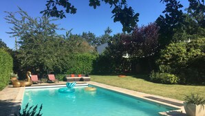 A swimming pool with a curved edge, surrounded by a patio area with outdoor furniture and a well-maintained lawn.