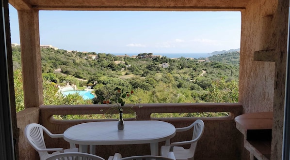 Enjoy a serene view of the lush landscape from this balcony, featuring a table for two and a beautiful view of the pool and surrounding hills.