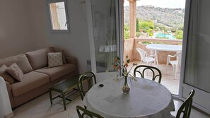 Relax in this inviting living area with a sofa, dining table, and patio access to a pool and lush greenery.