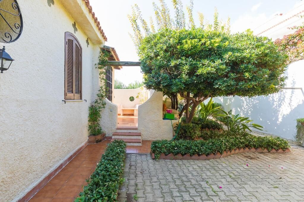 A paved courtyard with a small tree, a wall-mounted light fixture, and a window with shutters.