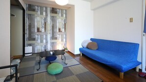 Una sala de estar con un sofá azul, una mesa de centro negra, un otoman verde y una pieza de arte de madera en la pared.