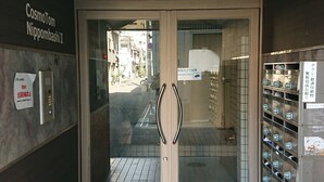 Entrada de un edificio con puerta de vidrio, un área de taquillas metálicas a la derecha y un cartel sobre la puerta.