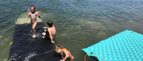 Une jetée qui s’avance dans un lac, avec un radeau gonflable bleu et une plateforme flottante noire.