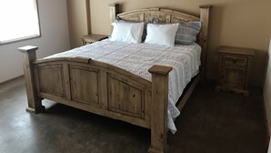 A wooden bed with a quilted cover, two bedside tables, and a window on the left. - Cabin 2 of 7 With Private River Access to the Nueces River (Uvalde)