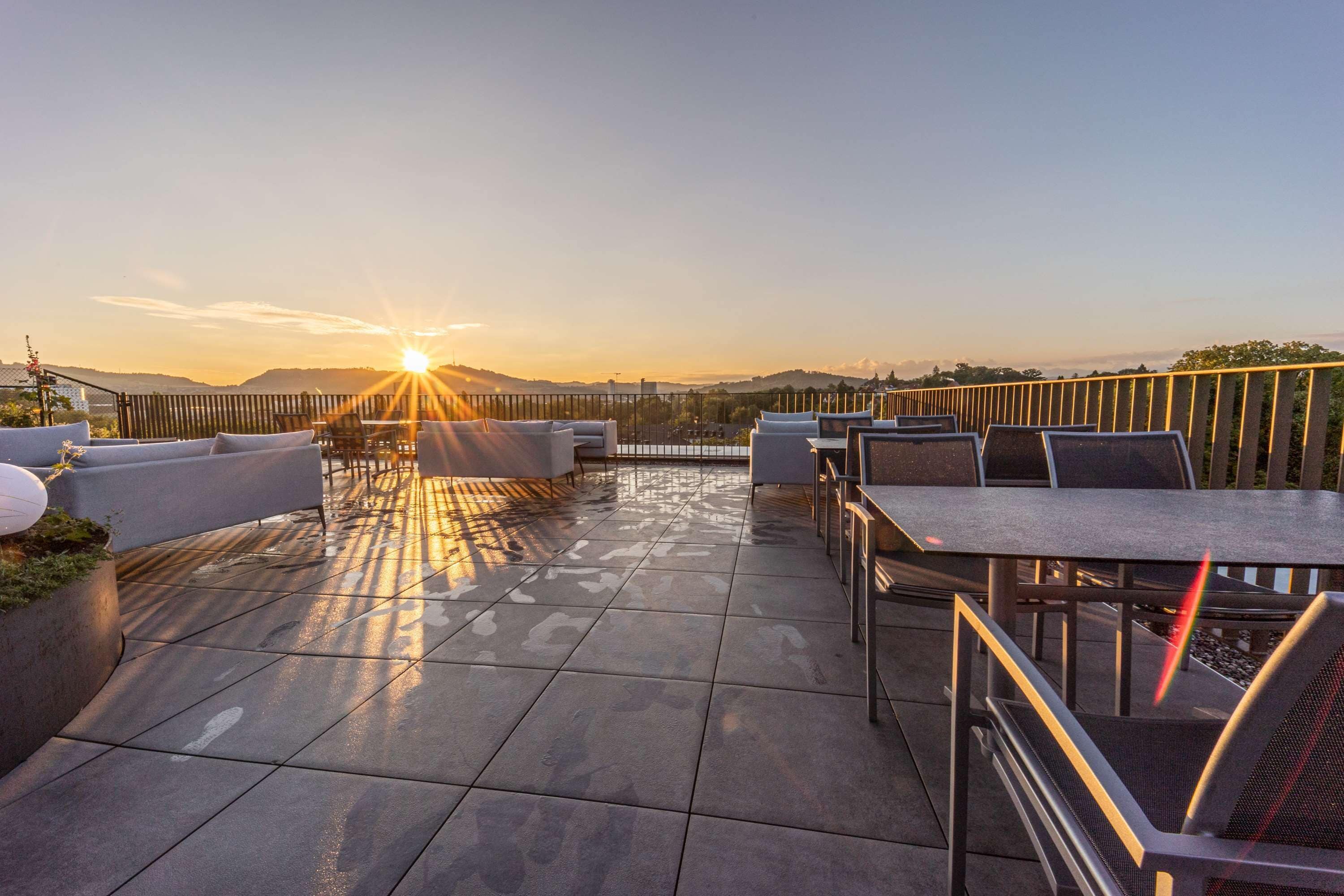 Un patio en la azotea con mesas al aire libre y vistas al atardecer.